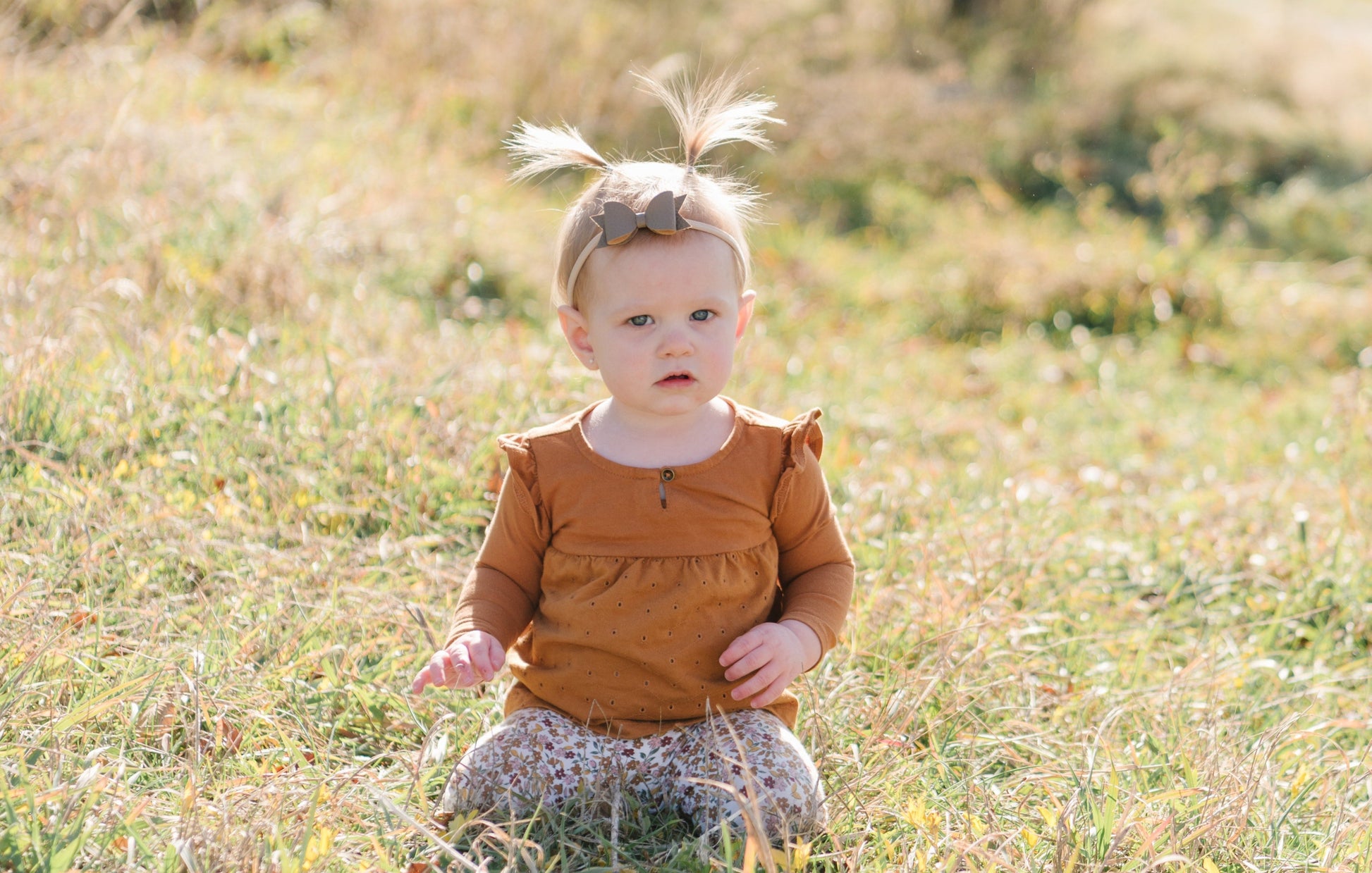 toddler sitting outside in grass with mini bow headband on, color tumbleweed